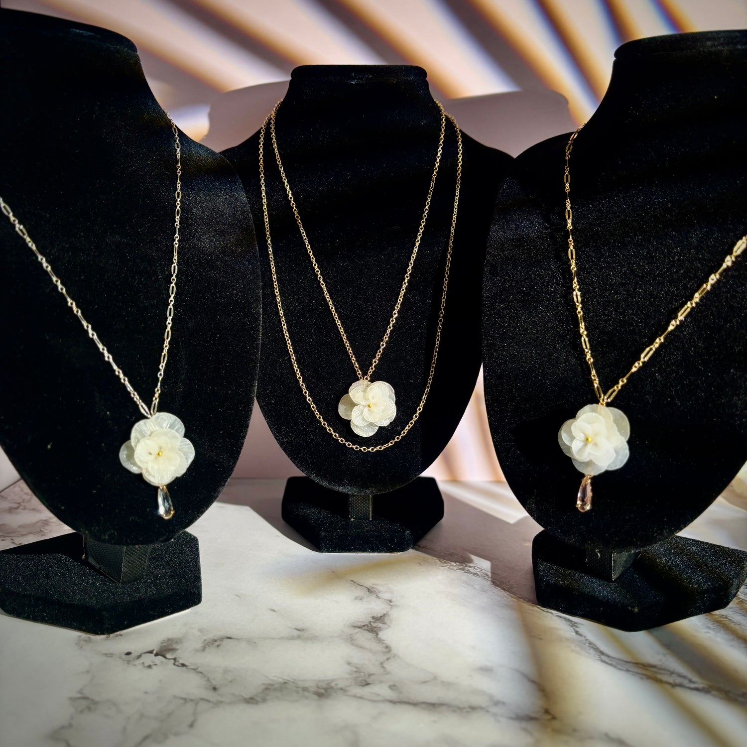 Handcrafted white flower pendants on gold and sterling silver chain necklaces, lightweight and hypoallergenic jewelry, displayed on black velvet stands.